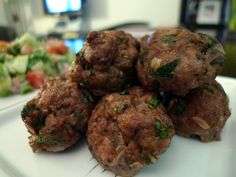 some meatballs are sitting on a white plate next to a green salad and television