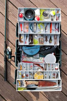 a fishing tackle box filled with lots of different types of fishing gear and accessories on top of a wooden deck