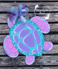 a purple and blue sea turtle with a bow on it's head sitting on a wooden plank