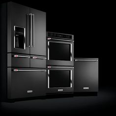 three ovens and two microwaves are shown in this black room with dark lighting