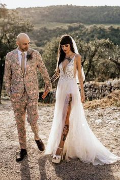 a man and woman in wedding attire walking on dirt ground with trees in the background