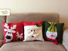 three christmas pillows sitting on top of a couch with santa claus and snowman faces