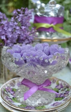 purple candies are in a glass bowl on a plate next to lavender flowers and tea cups