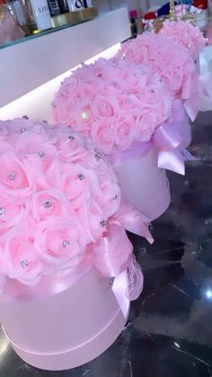 two pink roses are sitting in white vases on a counter top, one is decorated with crystals and the other has a bow