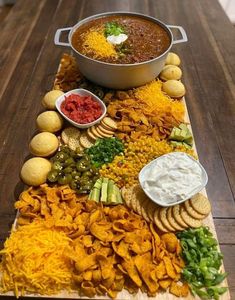 a platter filled with chips and dips on top of a wooden table next to a pot of chili