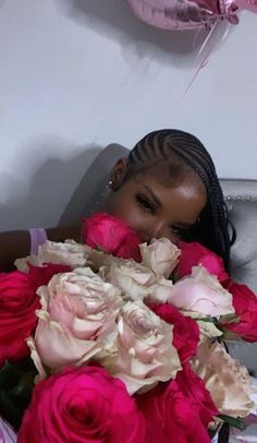 a woman with braids holding a large bouquet of pink and white roses in her hands