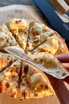 a person holding up a slice of pizza on a cutting board next to a knife