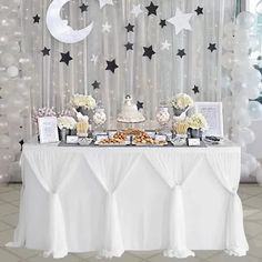 a table topped with cake and desserts next to a wall covered in white balloons