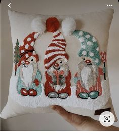 a hand holding a pillow with three gnomes on it and one is wearing a santa hat