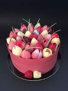 a pink bowl filled with lots of red and white tulips on top of a black table