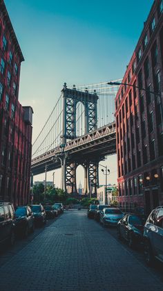 cars are parked on the street in front of some tall buildings and a large bridge