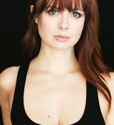 a close up of a woman with red hair wearing a black top and posing for the camera