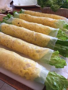 four burritos wrapped in paper sitting on a cutting board next to lettuce