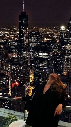 a woman sitting on top of a toilet in front of a cityscape at night