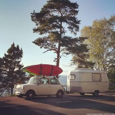 an old car with a surfboard strapped to it parked next to a camper