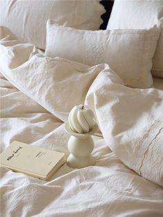 an unmade bed with white linens and a book on the pillowcase next to it