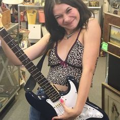 a woman is holding an electric guitar and posing for the camera in a store with other items