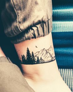 a person with a small tattoo on their arm that has trees and mountains in the background