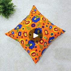 an orange pillow with blue and yellow flowers on it sitting next to a green plant