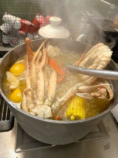 crab legs and corn are being cooked in a pot on the stove top with boiling water