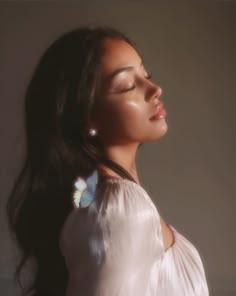 a woman with long dark hair wearing a white shirt and earrings, looking up at the sky