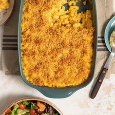 a casserole dish with cheese on top and salad in the bowl next to it