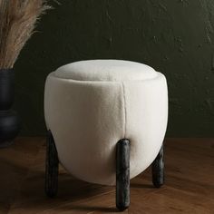 a white stool sitting on top of a wooden floor next to a plant in a vase