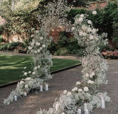 white flowers and candles are arranged on the ground in front of an arch with greenery