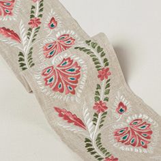 an embroidered ribbon with pink flowers and green leaves on beige linen, against a white background