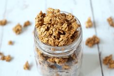 a glass jar filled with granola sitting on top of a white wooden table next to scattered oats