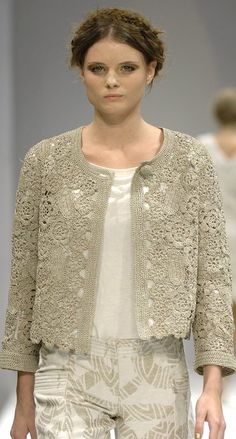 a woman is walking down the runway wearing white pants and a jacket with lace on it