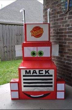 a red truck made out of cardboard sitting in front of a brick building with the words mack on it