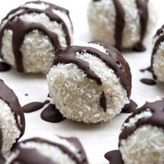 chocolate covered coconut balls are arranged on a white surface and drizzled with chocolate