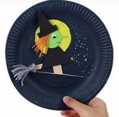 a hand holding a paper plate with a witch on it and a broom sticking out of it