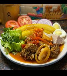 a white plate topped with meat and veggies covered in sauce next to sliced tomatoes