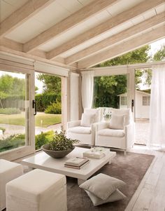 a living room filled with white furniture and lots of glass doors leading to an outside patio