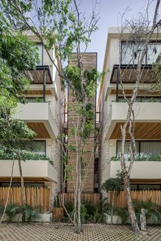 an apartment building with several balconies and trees in the front yard, surrounded by brick pavers