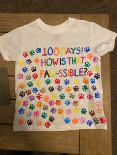 a white t - shirt with colorful paw prints on the front and back that says, 100 days howsith pa's possible?