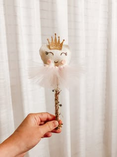 a hand holding a small doll with a crown on it's head and some flowers in the other hand