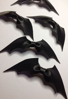 four black bats are shown on a white surface, one has a large bow at the top