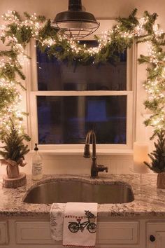 a kitchen sink under a window decorated with christmas lights and greenery on the windowsill