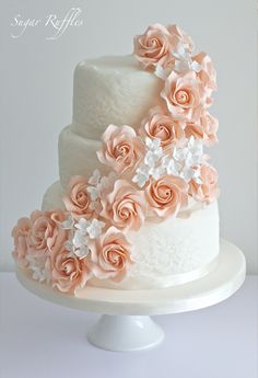 a wedding cake decorated with pink flowers on a white stand and the words sugar ruffles written in cursive writing