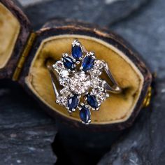 an antique ring with blue and white stones sits in its case on top of some rocks