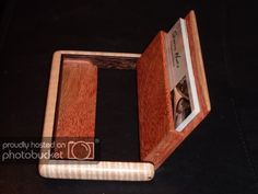 an open wooden box with a book inside on a black tableclothed surface and the cover is made out of wood