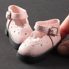 a hand holding a doll's pink shoes with holes on the bottom and black soles