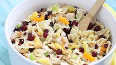 a white bowl filled with pasta salad on top of a blue cloth next to a wooden spoon