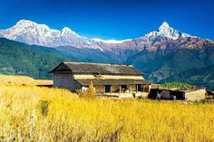 an old building in the middle of a field with mountains in the background