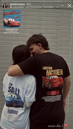 two people standing next to each other in front of a wall with cars on it