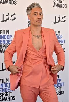 a man in an orange suit standing on a red carpet with his hands behind his back