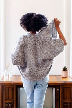 a woman standing in front of a tv with her back turned to the camera, wearing jeans and a sweater